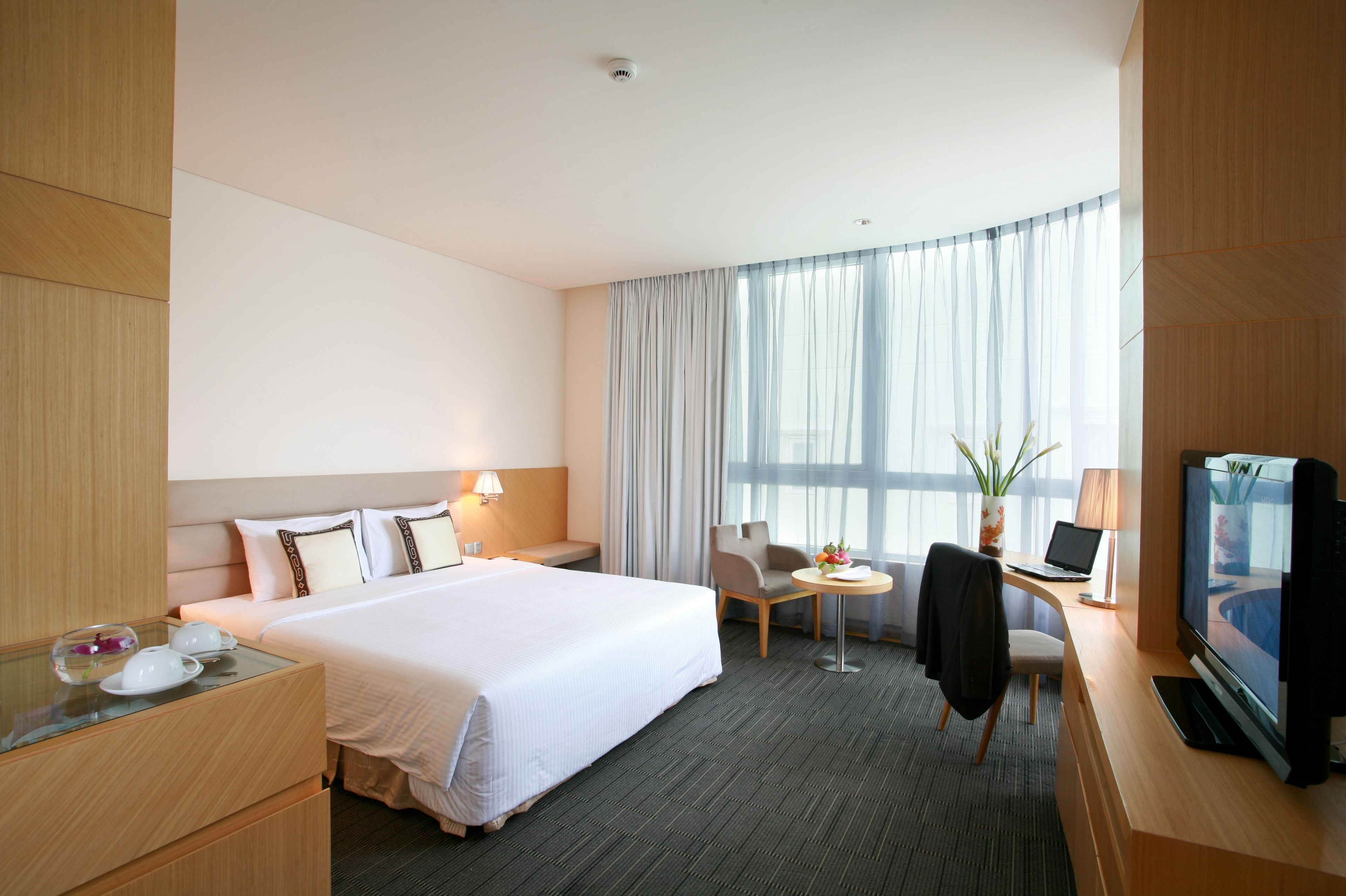 Une chambre d’hôtel avec un grand lit, un bureau avec un ordinateur portable, une télévision et une petite table avec une chaise.
