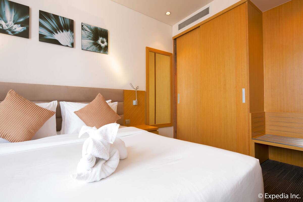 A hotel room with a large bed, wooden wardrobe, and artwork on the wall.