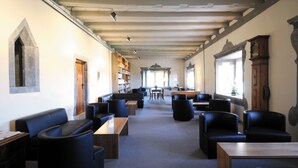 Una biblioteca con estanterías repletas de libros, asientos de cuero negro y techo de madera.