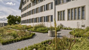 Un edificio de varios pisos con fachada simétrica, ventanas amplias y un sendero de grava que conduce a una jardinera de hormigón central.