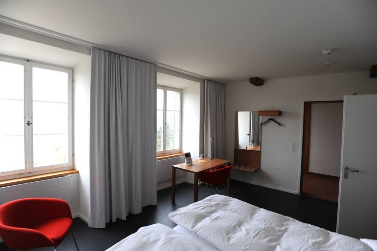 A hotel room with a bed, a desk, a chair, and a window with curtains.