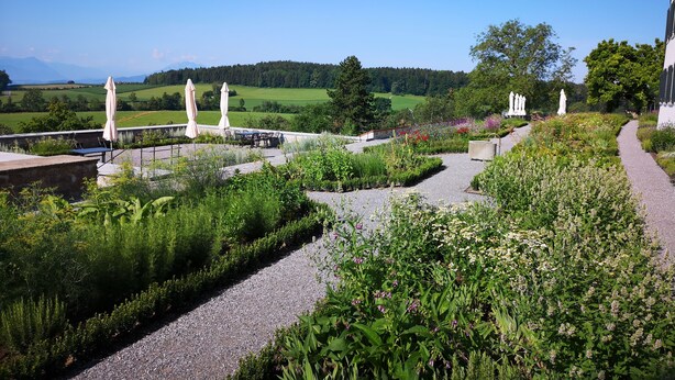 Un jardín con un sendero de grava, mobiliario exterior y vistas a un paisaje verde.