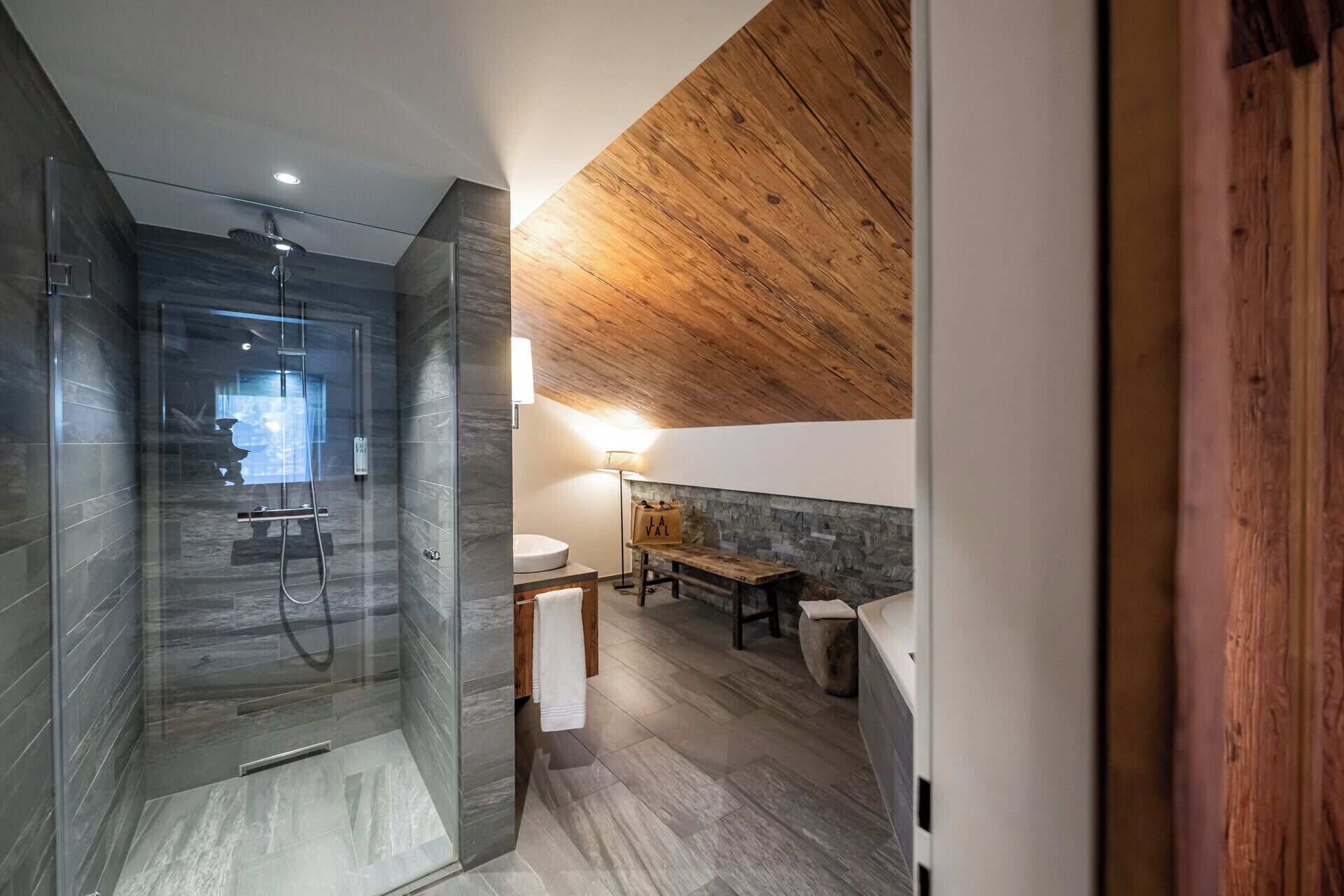 A modern bathroom with a glass-enclosed shower, a wooden ceiling, and a stone wall.