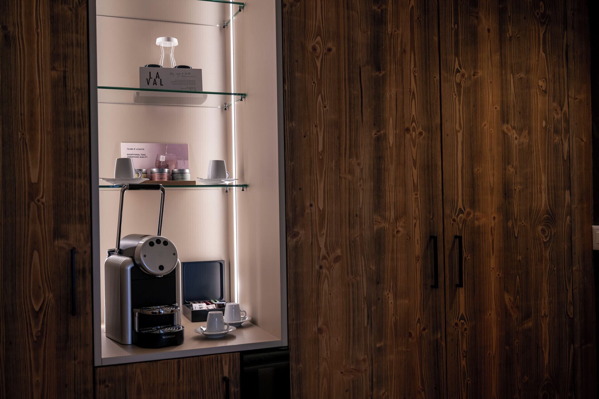A coffee station with a coffee machine, cups, and a glass display case containing tea and other items.