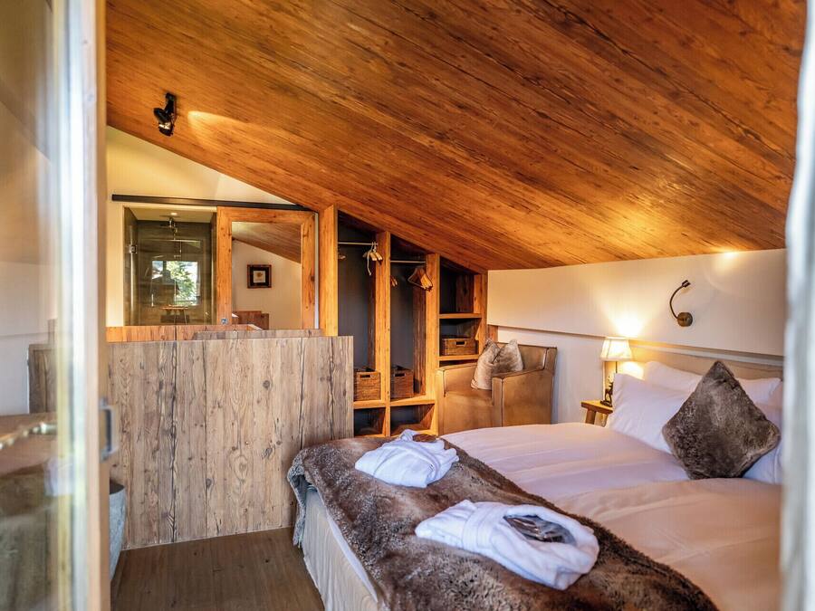 A cozy bedroom with a wooden ceiling, a large mirror, a wardrobe, and a bed with pillows and a blanket.
