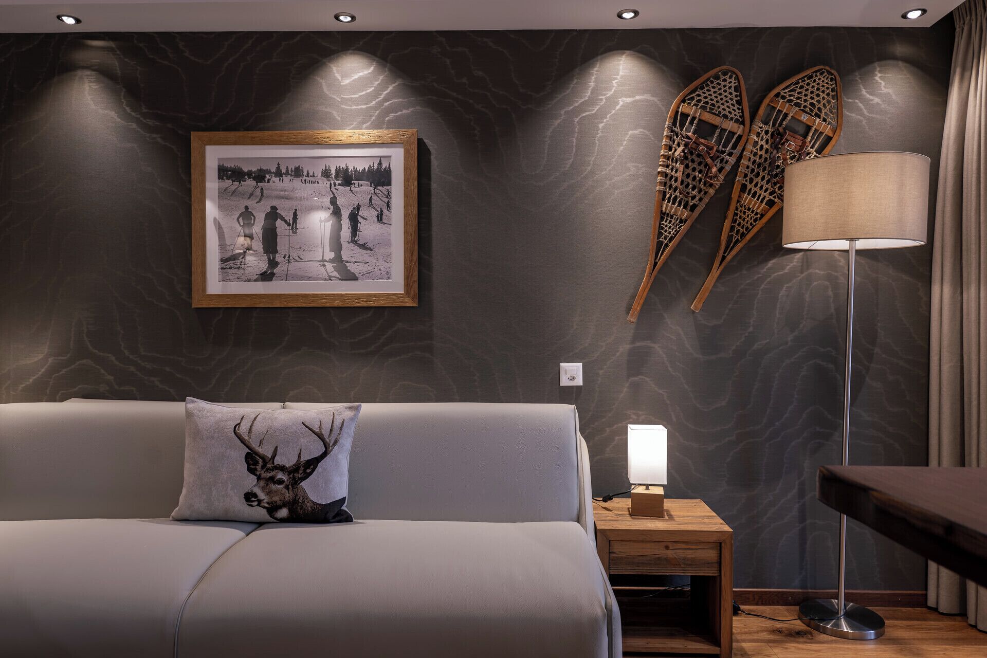 Un dormitorio moderno con un sofá gris, una fotografía enmarcadas en la pared, una lámpara y una mesita de noche de madera.