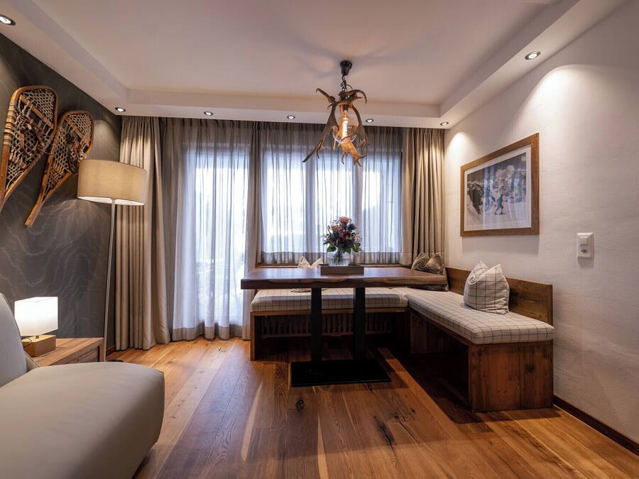 Una sala moderna con piso de madera, un comedor con un banco, un sofá, una lámpara y una araña.