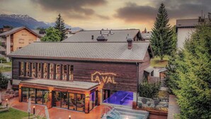 A modern building with a large glass facade, a swimming pool, and a wooden exterior. - La Val Hotel & Spa (Brigels)