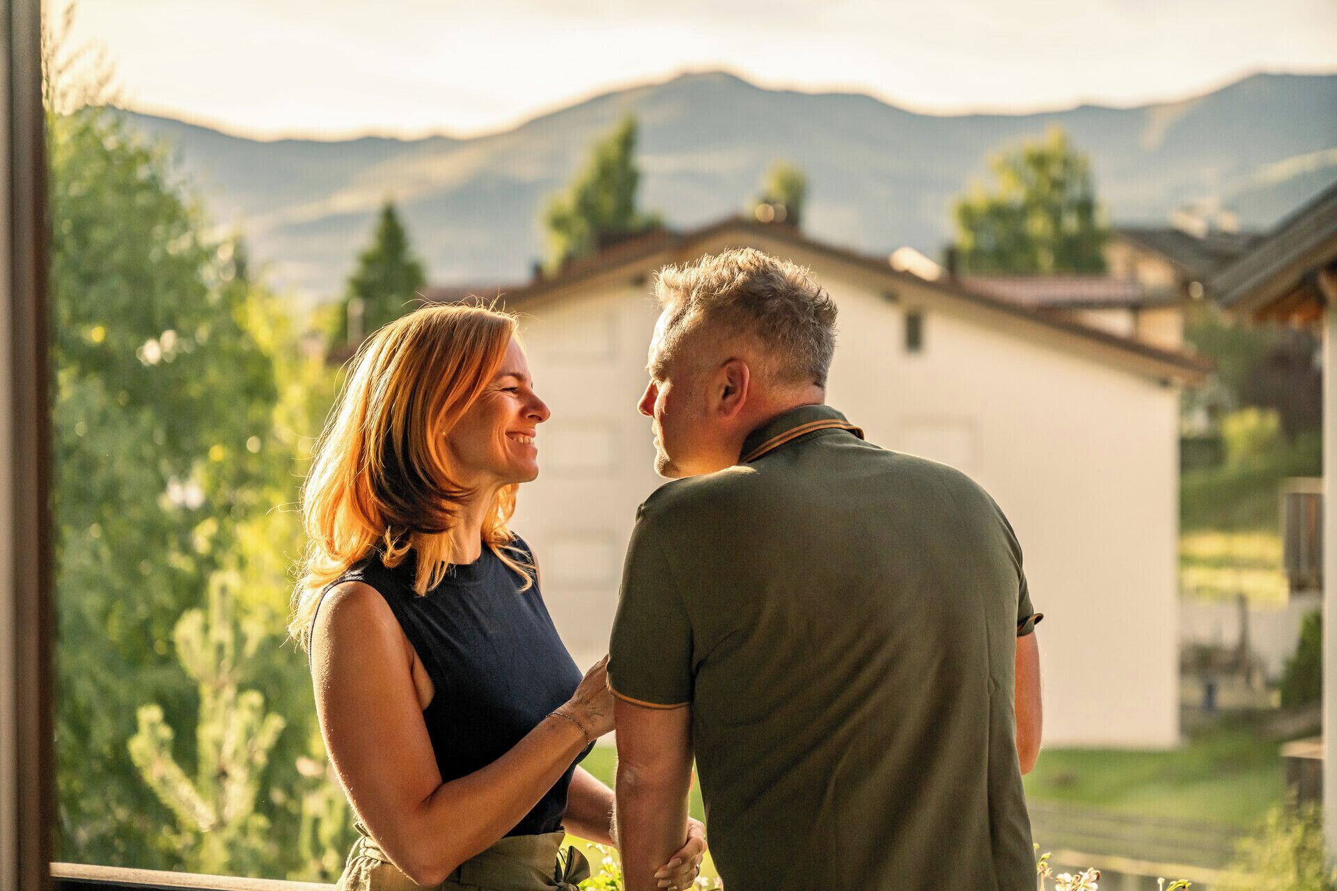 A couple standing indoors with a view of mountains and greenery outside.