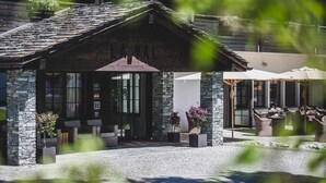 A stone building with a wooden roof, outdoor seating, and potted plants. - La Val Hotel & Spa (Brigels)