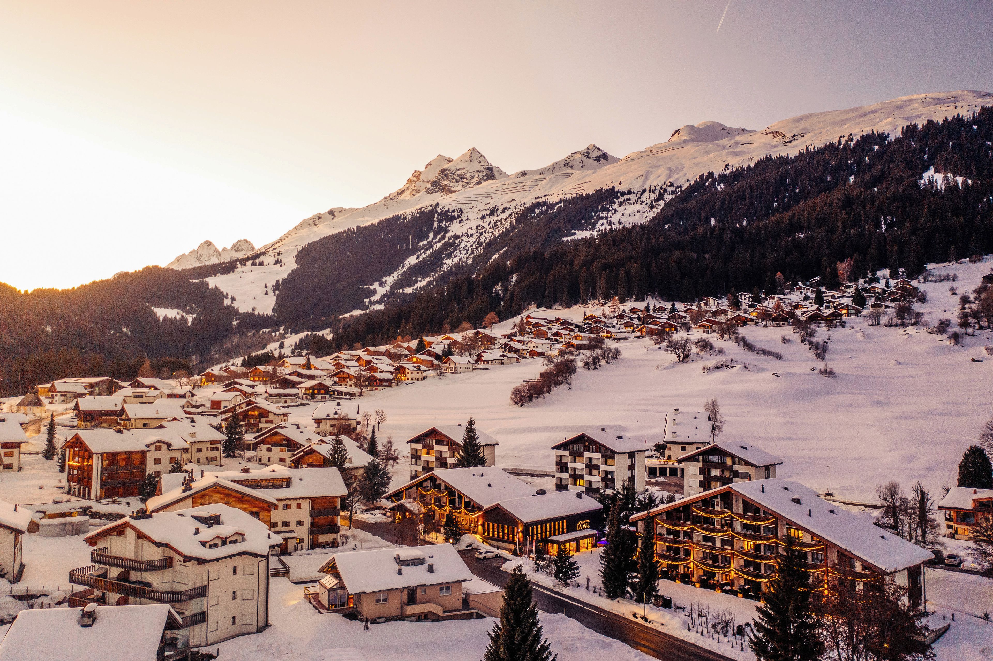 Eine verschneite Bergstadt mit Holzbauten und einer Skipiste.