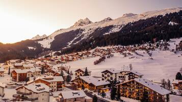 Eine verschneite Bergstadt mit Holzbauten und einer Skipiste.