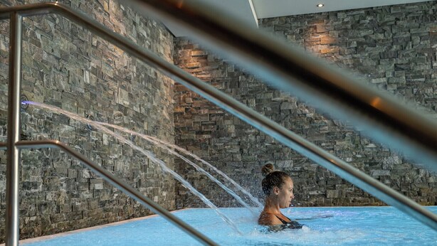 A person in a hot tub with water jets, surrounded by stone walls. - La Val Hotel & Spa (Brigels)