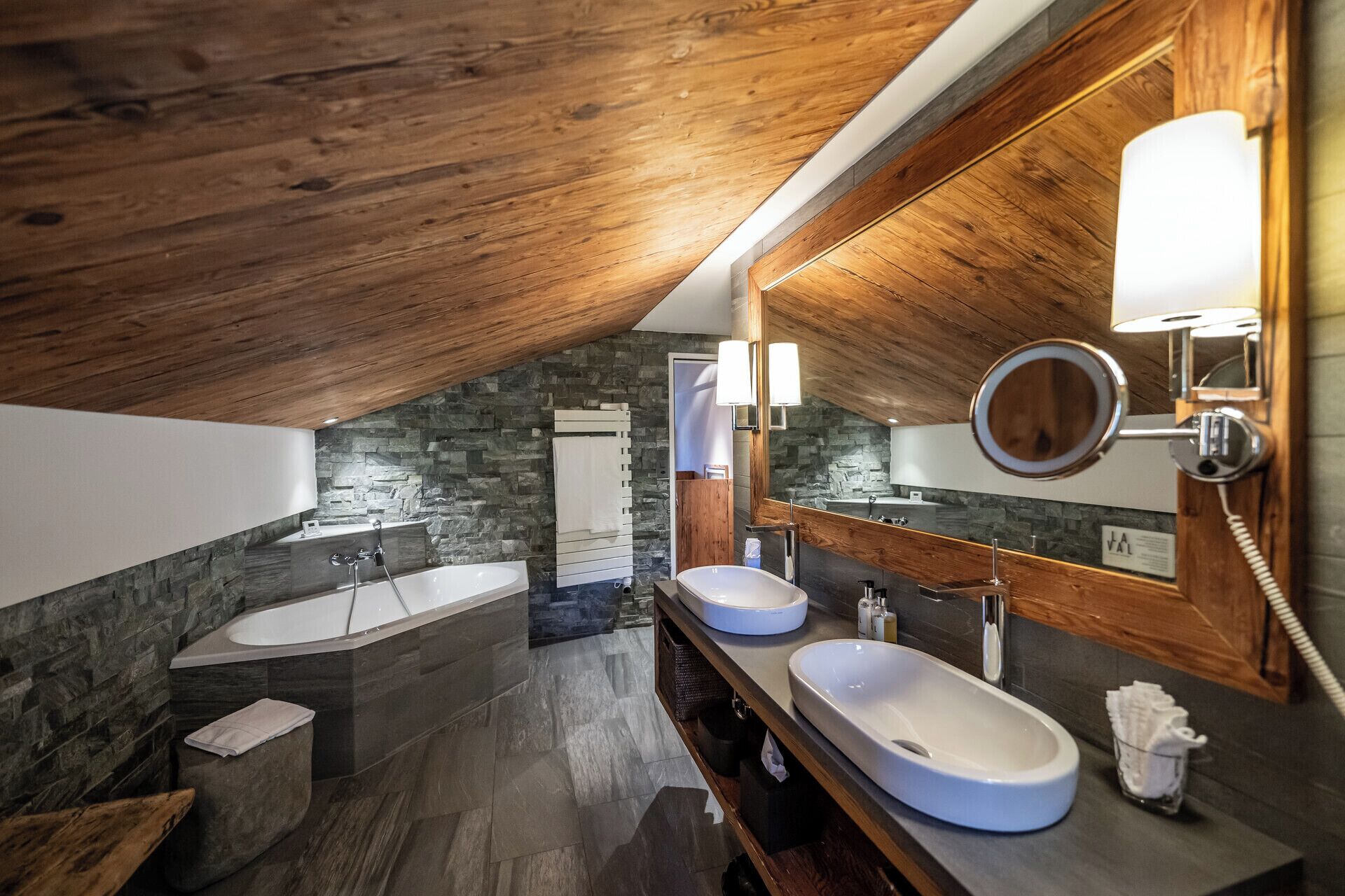 A modern bathroom with two sinks, a large bathtub, and a stone accent wall.
