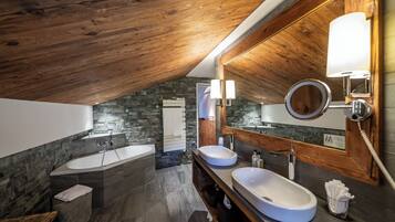 A modern bathroom with two sinks, a large bathtub, and a stone accent wall.