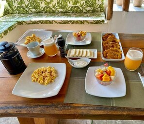 A breakfast table with various dishes including scrambled eggs, fruit, and beverages. - Hotel Playa Scondida Baru (Cartagena)
