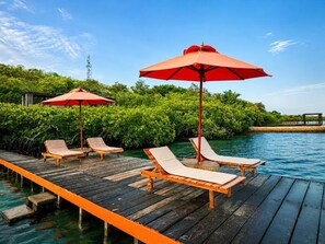 A wooden deck with lounge chairs and red umbrellas by a body of water. - Hotel PlayaScondida Baru (Cartagena)