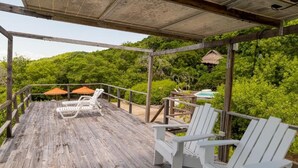 Une terrasse en bois avec des chaises blanches, une structure à toit de chaume et une végétation luxuriante en arrière-plan.