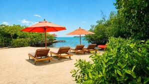 Une plage avec des chaises longues en bois et des parasols rouges, un ciel bleu dégagé et une vue sur la mer.