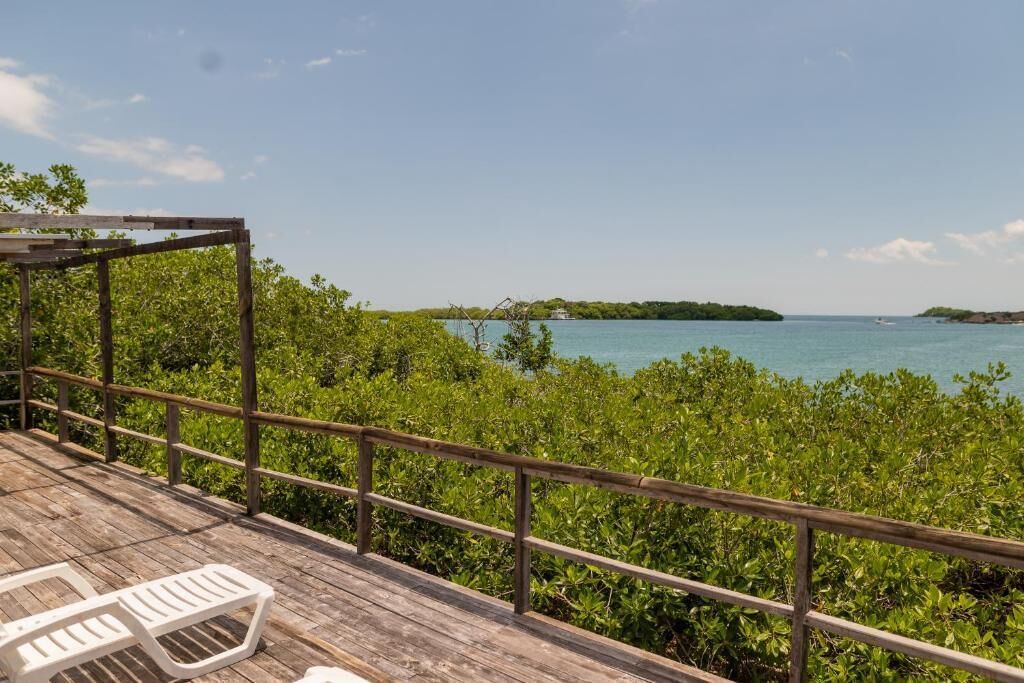 A wooden deck with a railing, a covered area, and a view of the sea and islands.