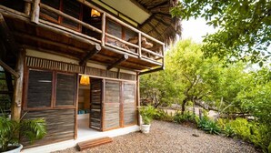 Une maison en bois à deux étages, dotée d’un balcon, entourée d’une allée gravillonnée et d’une végétation luxuriante.