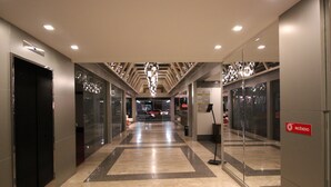 Un pasillo moderno de hotel con puertas de vidrio, suelo de mármol e iluminación geométrica en el techo.