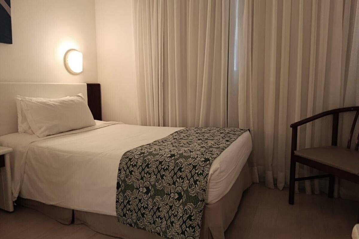 Une chambre d’hôtel comprenant un lit, une table de chevet, une chaise et une lampe fixée au mur.