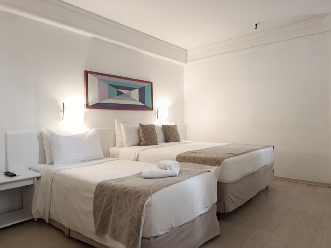 Una habitación de hotel con dos camas, una mesita de noche con lámpara y un cuadro en la pared.