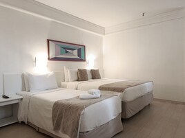 Una habitación de hotel con dos camas, una mesita de noche con lámpara y un cuadro en la pared.