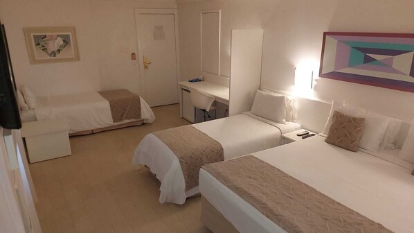 A hotel room with two single beds, a desk, a chair, and a small table.