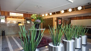 Un vestíbulo con mostrador de recepción, plantas en macetas y una alfombra estampada.
