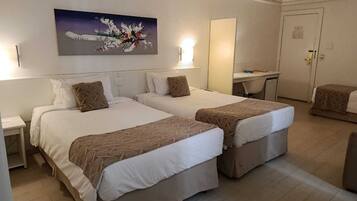A hotel room with two beds, a desk, a chair, and a painting on the wall.