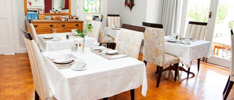 A dining area with a wooden floor, white tablecloths, and floral chairs.