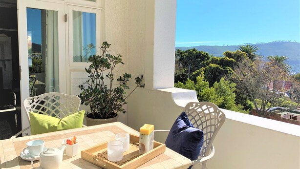 A balcony with a table set for two, a potted plant, and a view of the landscape.