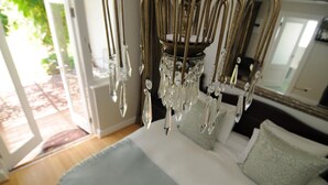 A bedroom with a chandelier, a bed with white bedding, and a view of the outdoors through a glass door.