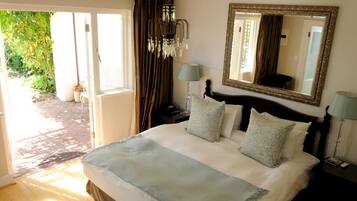 A bedroom with a large bed, a chandelier, a mirror, and a view of the outdoors.