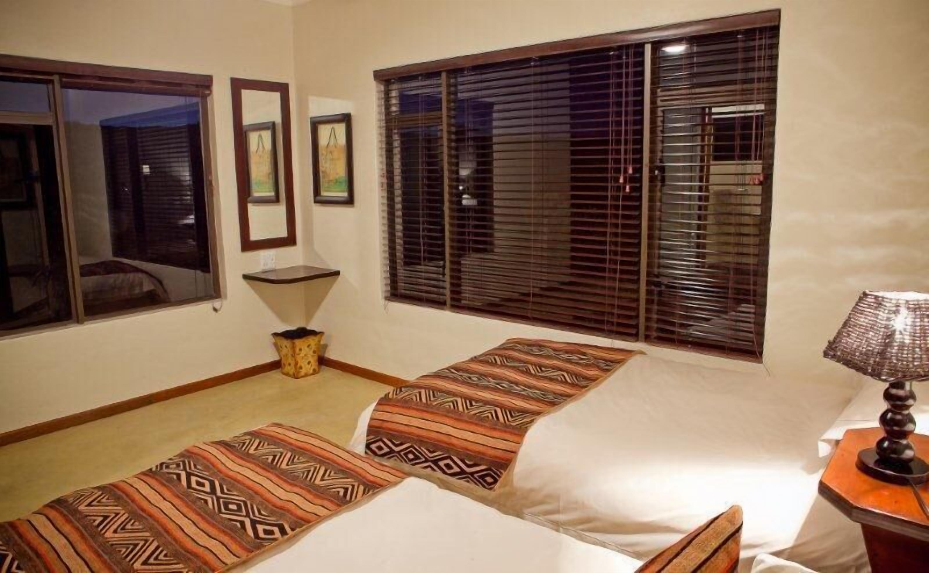 Habitación de hotel con dos camas, una mesita, una lámpara y una ventana con persianas.