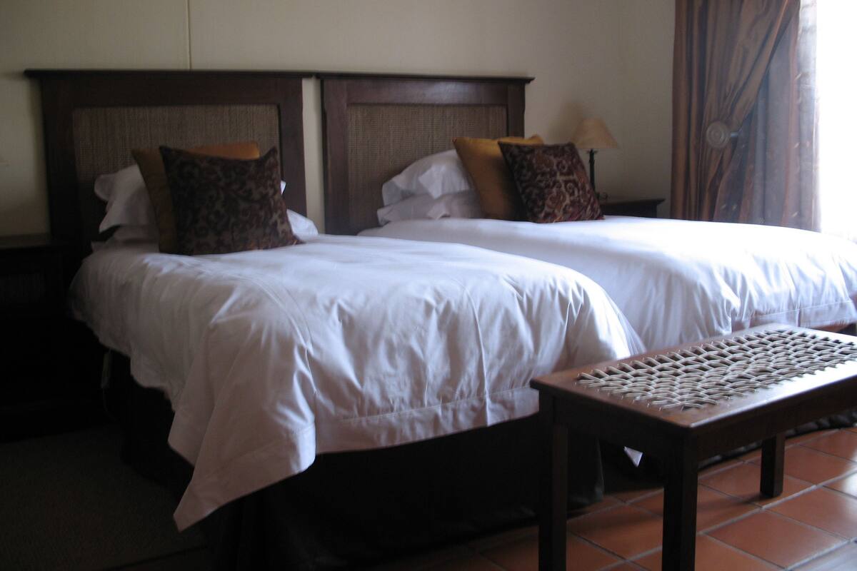Een hotelkamer met twee bedden, een nachtkastje, een lamp en een geweven tafel.