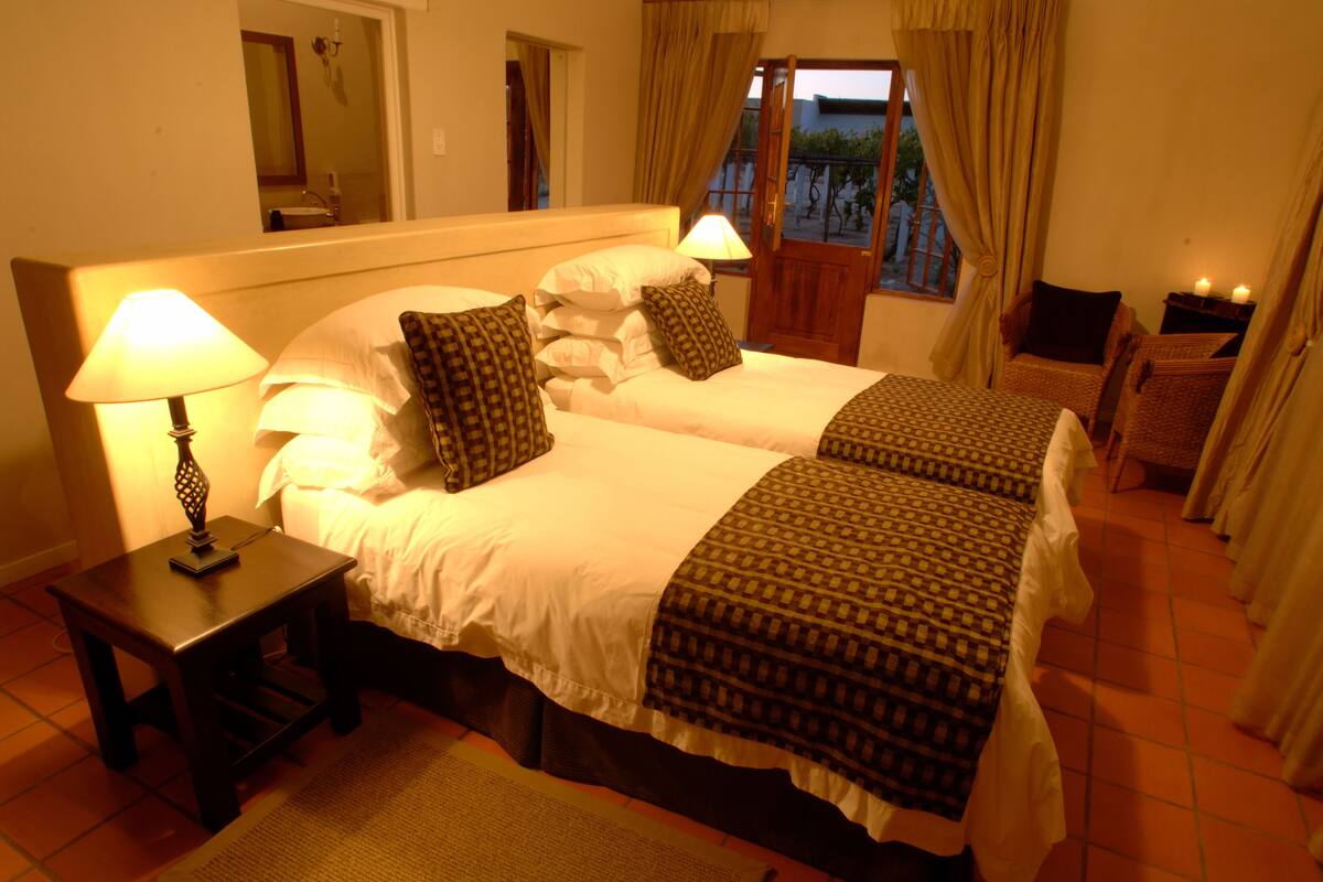 Een tweepersoonsbed met een gebedruid sprei, twee bedlampjes en een nachtkastje met lamp.