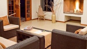 Un salon chaleureux, doté de meubles en osier, d’une cheminée et d’une porte-fenêtre coulissante donnant sur un espace extérieur.