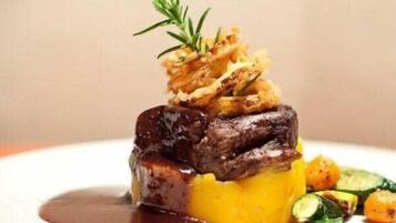 A plated dish with a piece of meat, a yellow base, and vegetables.