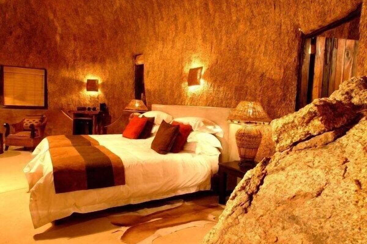 Een kamer met een bed, twee nachtkastjes, een stoel en een grote rots.