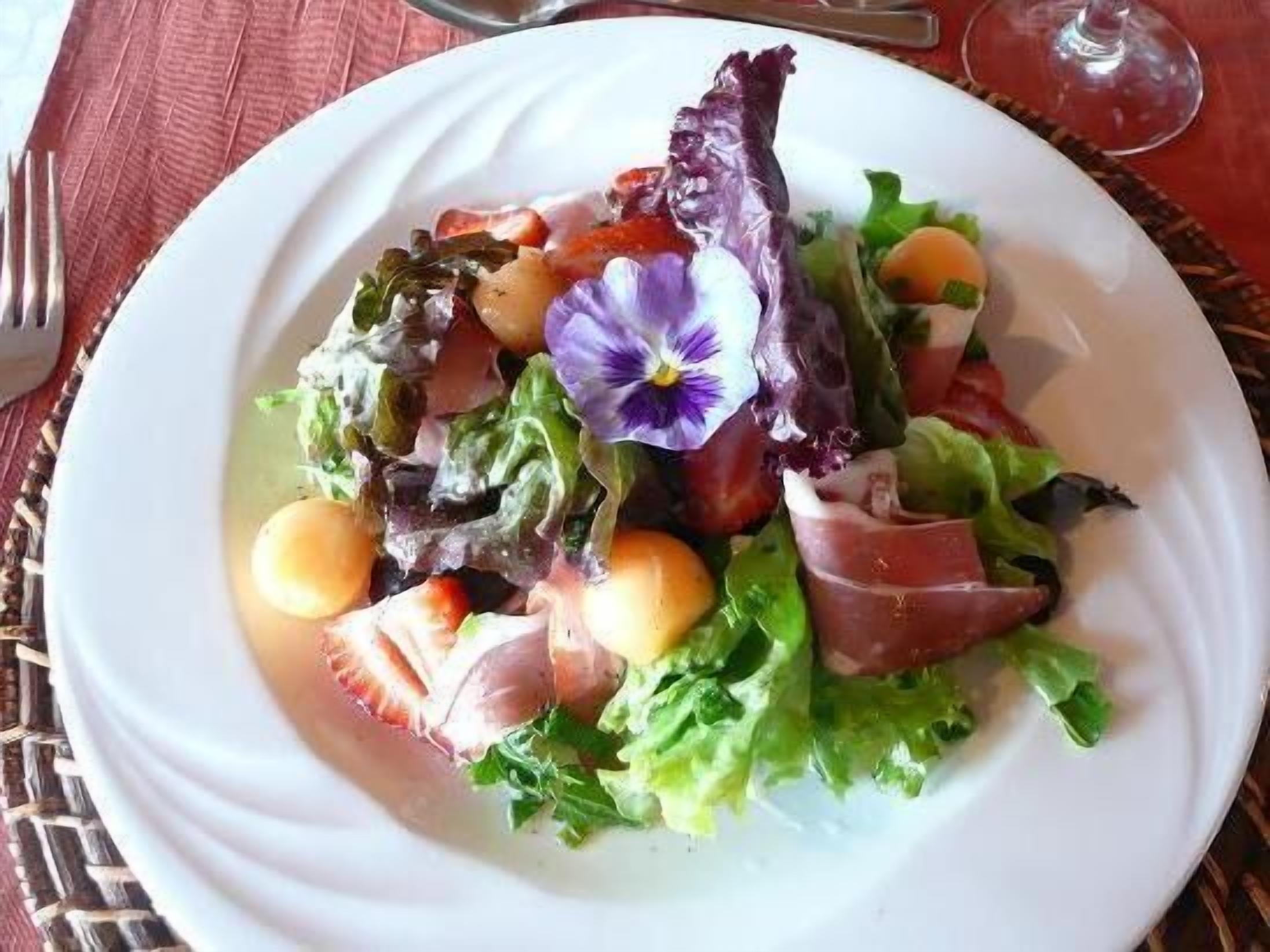 Une assiette de salade composée et de légumes, agrémentée d’une fleur violette.