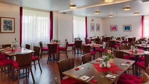Un espace repas comprenant plusieurs tables et chaises, chacune étant recouverte d’une nappe et agrémentée de serviettes rouges.