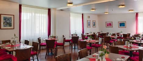 A dining area with multiple tables and chairs, each set with red tablecloths and napkins.