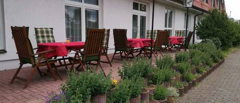 A row of outdoor tables with chairs, a brick pathway, and flower planters along the side.