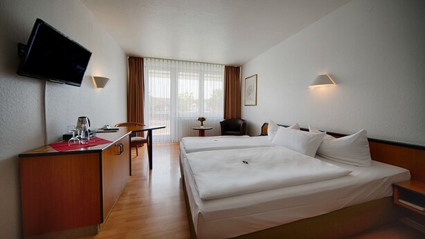 Une chambre d’hôtel avec un lit, un bureau, une chaise, une télévision et une fenêtre avec des rideaux.