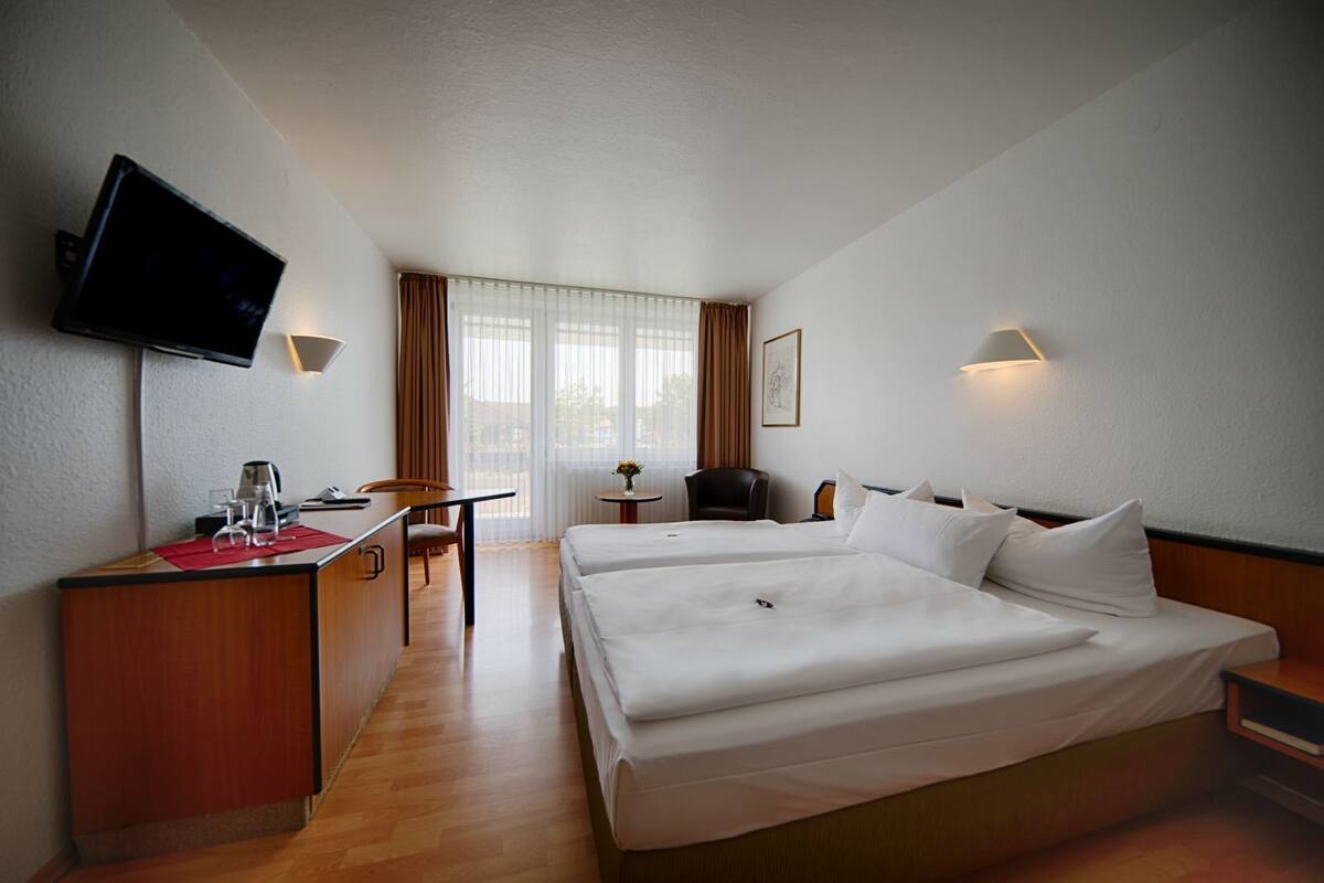 Een hotelkamer met een bed, een bureau, een stoel, een televisie en een raam met gordijnen.