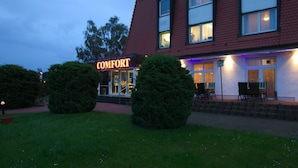 Un hôtel avec une enseigne indiquant « CONFORT », de grandes fenêtres et un espace extérieur bien aménagé et bien éclairé.