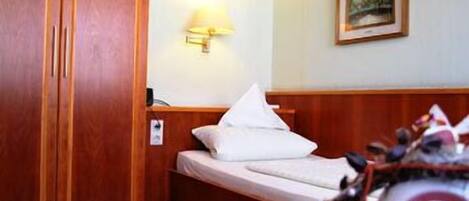 Ein Hotelzimmer mit einem Bett, einem Nachttisch, einer Lampe, einem Holzschrank und einem gerahmten Bild an der Wand.